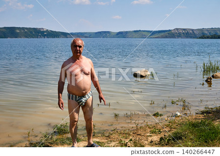 Cheerful elderly pensioner loves to swim in the summer river Cheerful elderly pensioner loves to swim in the summer river 140266447
