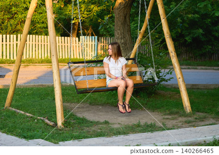 Young attractive woman sits on swing waiting near rural road Young attractive woman sits on swing waiting near rural road 140266465