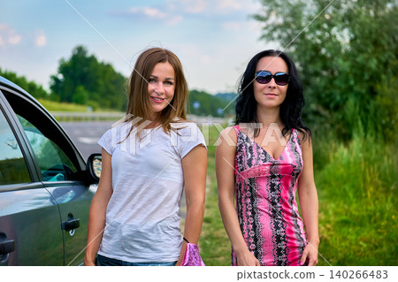 Two young cheerful women near car on road during trip Two young cheerful women near car on road during trip 140266483
