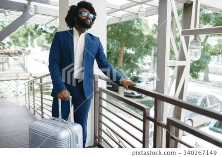 Black man in formal suit with packed suitcase entering hotel door Black man in formal suit with packed suitcase entering hotel door 140267149