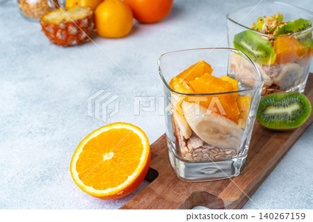 Glass with fruit pieces and oatmeal muesli on wooden board 140267159
