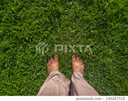 Legs and feet of a person connecting with nature, standing barefoot on soft, lush green grass, fostering a sense of grounding, relaxation, and wellness outdoors under the natural light Legs and feet of a person connecting with nature, standing barefoot on soft, lush green grass, fostering a sense of grounding, relaxation, and wellness outdoors under the natural light 140267328
