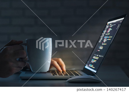Coding session with coffee in a dimly lit room at night on a laptop 140267417