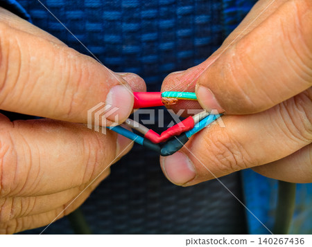 Worker hands carefully joining multiple colored electrical wires with heat shrink tubing, symbolizing connection, repair, and professional installation for various systems. Worker hands carefully joining multiple colored electrical wires with heat shrink tubing, symbolizing connection, repair, and professional installation for various systems. 140267436