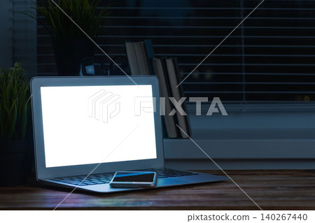 Workstation setup with laptop and smartphone at night near the window and bookshelf 140267440
