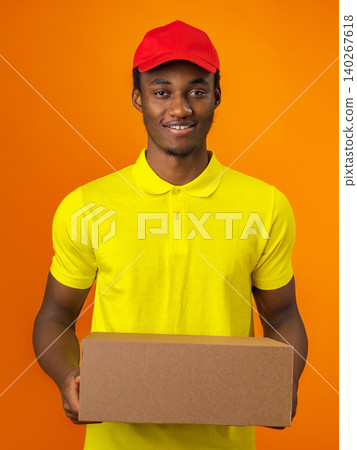 Delivery worker holds a box with a smile against an orange background in bright clothing Delivery worker holds a box with a smile against an orange background in bright clothing 140267618