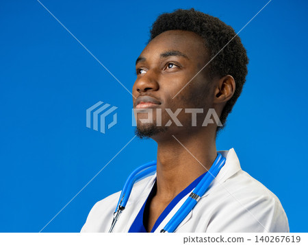 Young doctor with a stethoscope looking up while posing against a blue background 140267619
