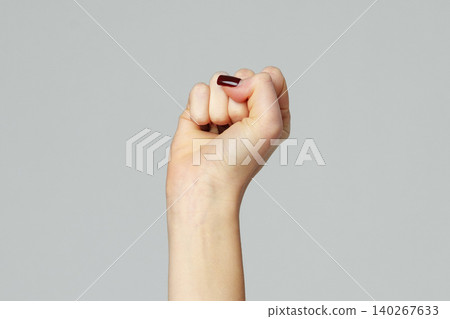Hand shows a raised fist with a dark nail polish against a plain background Hand shows a raised fist with a dark nail polish against a plain background 140267633