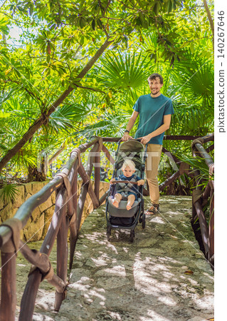 Dad walks with an infant stroller through dense tropical greenery, showing family travel, fatherhood, eco park visit and vacation routine concept Dad walks with an infant stroller through dense tropical greenery, showing family travel, fatherhood, eco park visit and vacation routine concept 140267646