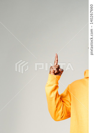 Person raises one finger while wearing a yellow hoodie against a plain background Person raises one finger while wearing a yellow hoodie against a plain background 140267660