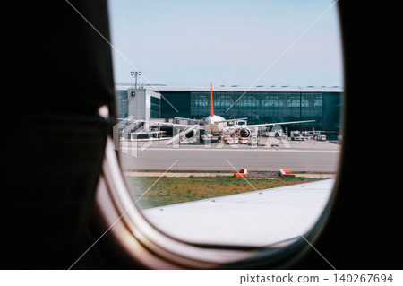 View from airplane window showing airport and parked aircraft in clear weather 140267694