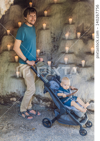 Dad walks with an infant stroller inside a dim grotto with many candles, showing family travel, atmosphere, faith and cultural experience concept Dad walks with an infant stroller inside a dim grotto with many candles, showing family travel, atmosphere, faith and cultural experience concept 140267756