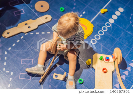 Three year old toddler sitting alone and playing with wooden learning toy at science center, early STEM education, curiosity and child development concept 140267801