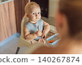 Infant practices self feeding with vegetables in a kitchen, showing baby led weaning, early nutrition and family care concept 140267874