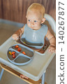 Infant practices self feeding with vegetables in a kitchen, showing baby led weaning, early nutrition and family care concept 140267877