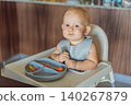 Infant practices self feeding with vegetables in a kitchen, showing baby led weaning, early nutrition and family care concept 140267879