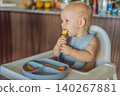 Infant practices self feeding with vegetables in a kitchen, showing baby led weaning, early nutrition and family care concept 140267881