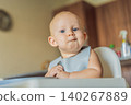 Infant practices self feeding with vegetables in a kitchen, showing baby led weaning, early nutrition and family care concept 140267889
