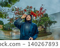 Adult man faces heavy rain and strong wind near palm trees and city buildings, showing storm weather, hurricane season and climate resilience concept 140267893