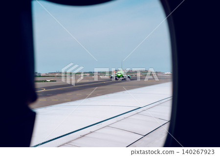 View of a green airplane taxiing on the runway from the window of another airplane View of a green airplane taxiing on the runway from the window of another airplane 140267923