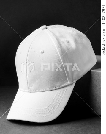 White cap placed on a dark surface next to a light-colored box White cap placed on a dark surface next to a light-colored box 140267971