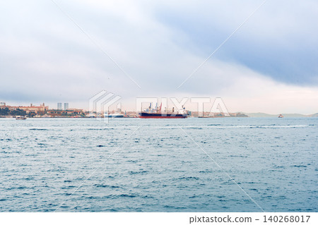 Cargo ship sails in the harbor during cloudy weather with city skyline in view Cargo ship sails in the harbor during cloudy weather with city skyline in view 140268017