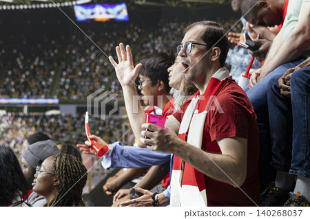 Tense football supporters reacting to a dramatic final minute attack during live soccer match in crowded stadium stands with scarf and vuvuzela energy. Anticipation dominate the decisive moment. Tense football supporters reacting to a dramatic final minute attack during live soccer match in crowded stadium stands with scarf and vuvuzela energy. Anticipation dominate the decisive moment. 140268037