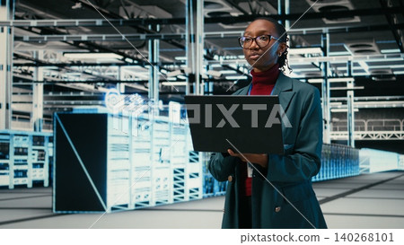 Female programmer walking in data center uses AR simulation and laptop to monitor systems. African american woman in server hub uses notebook to do optimizations, VFX compositing, camera A Female programmer walking in data center uses AR simulation and laptop to monitor systems. African american woman in server hub uses notebook to do optimizations, VFX compositing, camera A 140268101