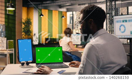 Vertical blue screen and green screen on laptop with black man, reviewing data analysis and business intel. Professional office activity, visual data and reports assist with resource allocation. Vertical blue screen and green screen on laptop with black man, reviewing data analysis and business intel. Professional office activity, visual data and reports assist with resource allocation. 140268150