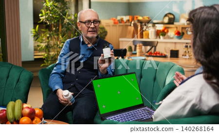 Chroma key screen on laptop held by old physician during in-home routine checkup, conducting health exam for senior man. Doctor conducting assisted living and preventive treatment. Chroma key screen on laptop held by old physician during in-home routine checkup, conducting health exam for senior man. Doctor conducting assisted living and preventive treatment. 140268164