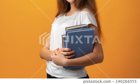 Student holds blue folders against a bright orange background in a studio setting Student holds blue folders against a bright orange background in a studio setting 140268355