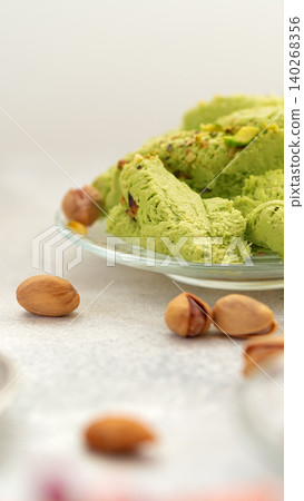 Green dessert with chopped nuts on a plate beside whole nuts on a light surface Green dessert with chopped nuts on a plate beside whole nuts on a light surface 140268356