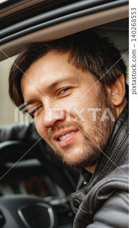 Man sitting in car with a smile and leather jacket during the day Man sitting in car with a smile and leather jacket during the day 140268553