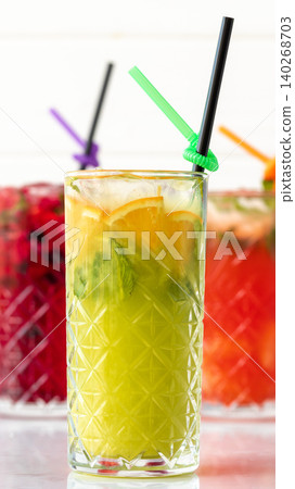 Fresh fruit drink served in a clear glass with colorful straws at a summer gathering 140268703