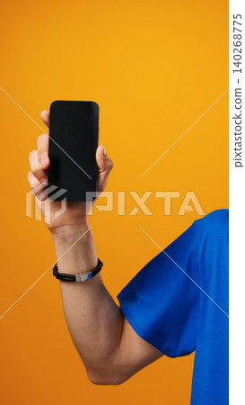 Person holds smartphone against bright orange background in indoor setting 140268775