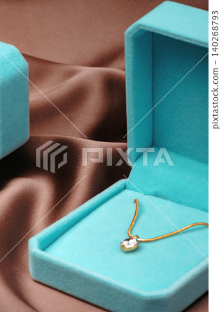 Necklace and jewelry box placed on a brown fabric surface for display during daytime 140268793