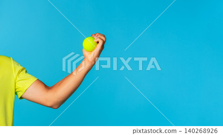 Person holds a green tennis ball against a blue background near a bright light source Person holds a green tennis ball against a blue background near a bright light source 140268926