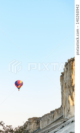 Hot air balloon floats above rocky cliffs during clear sky in the early morning light 140268942