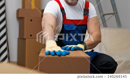 Worker in blue and red outfit moves cardboard box in storage area 140269145