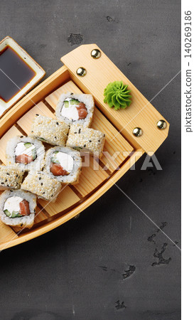 Sushi served on a wooden boat with soy sauce and wasabi on a dark table Sushi served on a wooden boat with soy sauce and wasabi on a dark table 140269186