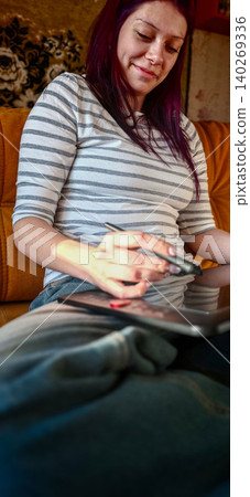 Teenage girl with purple hair draws on a graphic tablet while sitting on a couch, wearing a striped shirt and relaxed pants in a cozy indoor setting Teenage girl with purple hair draws on a graphic tablet while sitting on a couch, wearing a striped shirt and relaxed pants in a cozy indoor setting 140269336