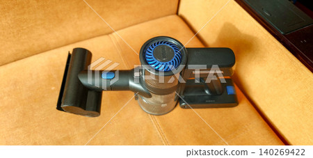 Handheld vacuum cleaner with blue accents placed on a tan upholstered surface, showcasing its sleek design and compact size for easy storage and use Handheld vacuum cleaner with blue accents placed on a tan upholstered surface, showcasing its sleek design and compact size for easy storage and use 140269422