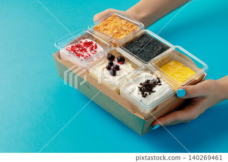 Mousse desserts in square plastic boxes with different toppings on pink table 140269461