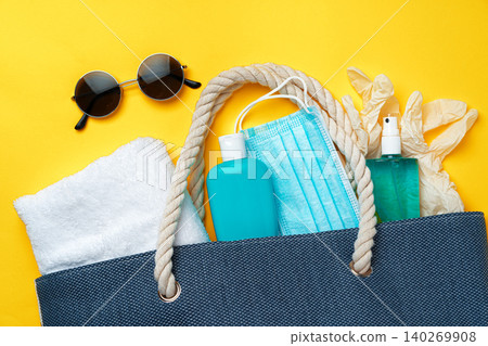 Blue beach bag with beach accessories and protective mask on yellow background Blue beach bag with beach accessories and protective mask on yellow background 140269908