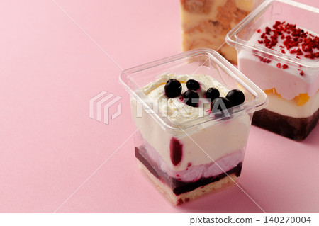 Mousse desserts in square plastic boxes with different toppings on pink table Mousse desserts in square plastic boxes with different toppings on pink table 140270004