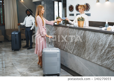 Young attractive woman with packed suitcase standing in hotel lobby Young attractive woman with packed suitcase standing in hotel lobby 140270055