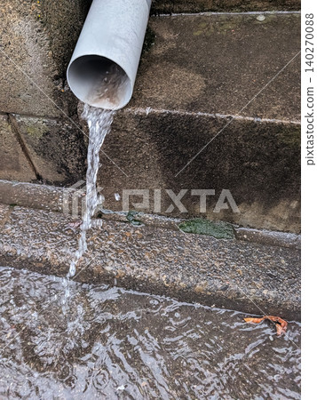 A drainpipe forcefully discharging rainwater and a wet road surface / Image of heavy rain, disaster prevention, and drainage equipment A drainpipe forcefully discharging rainwater and a wet road surface / Image of heavy rain, disaster prevention, and drainage equipment 140270088