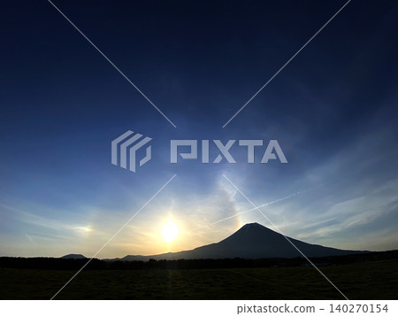富士山旁冉冉升起的太陽反射在薄薄的雲層上,形成一道弧形彩虹,彷彿從富士山頂升起。 富士山旁冉冉升起的太陽反射在薄薄的雲層上,形成一道弧形彩虹,彷彿從富士山頂升起。 140270154
