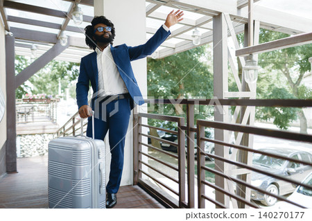 Black man in formal suit with packed suitcase entering hotel door 140270177