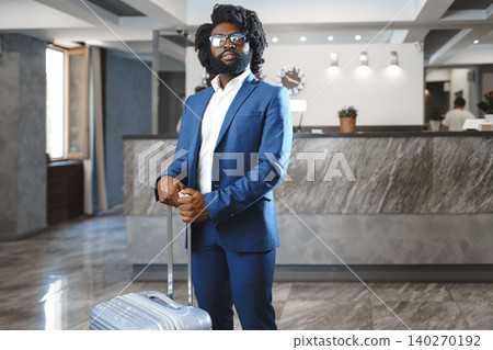 Black businessman with packed luggage standing in hotel lobby Black businessman with packed luggage standing in hotel lobby 140270192